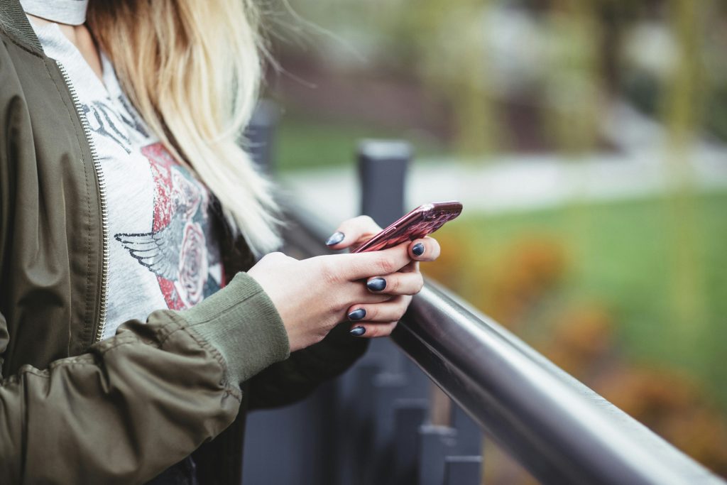 Woman standing outside, holding a smartphone, perhaps using a phone monitoring app for parents to track her kids' social media apps.