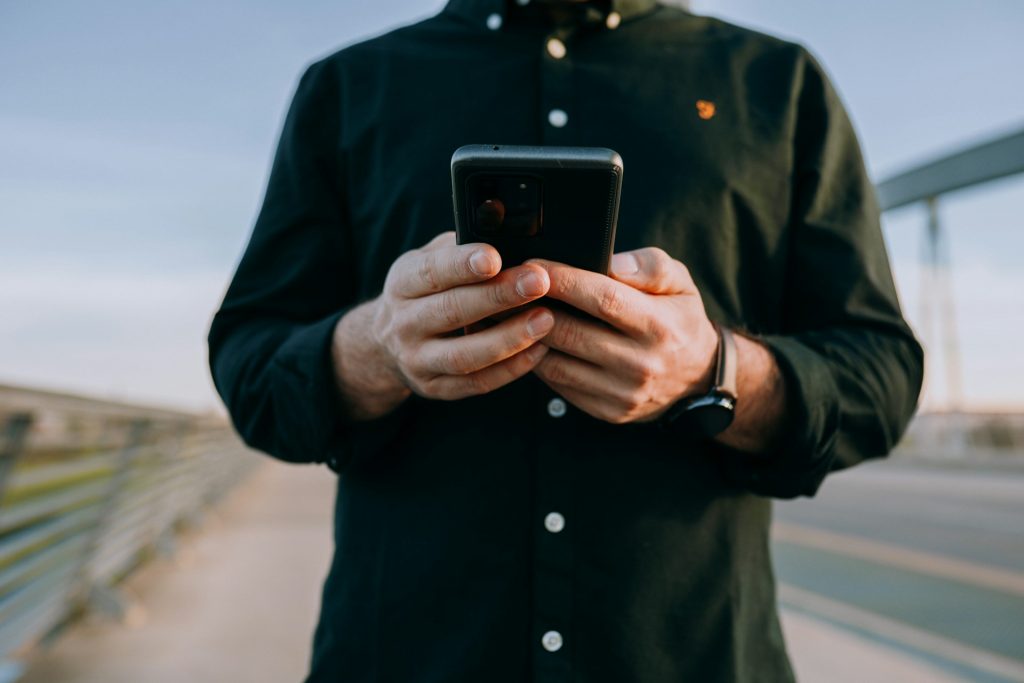 Man standing outside and holding a phone, perhaps monitoring his kids' social media apps.
