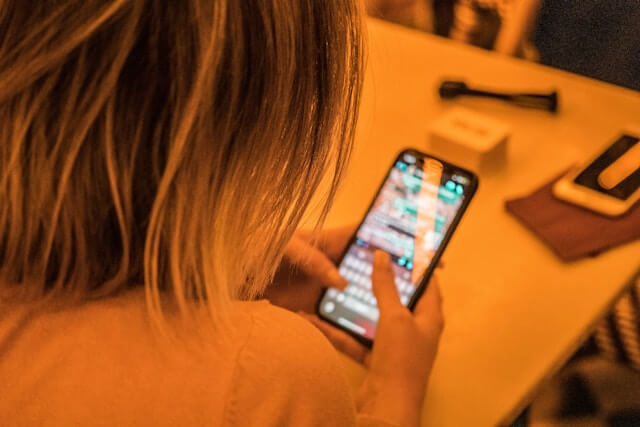 Picture taken from the back of a girl's head, over her shoulders. She is seen texting, possibly using texting acronyms. The phone display is blurred.