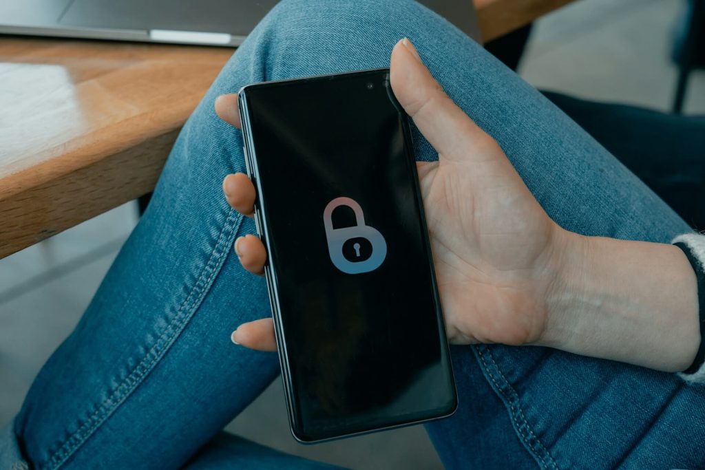 Girl holding a phone, on the display there's a lock symbol. The image represents data privacy concerns, one of the dangers of WhatsApp. 