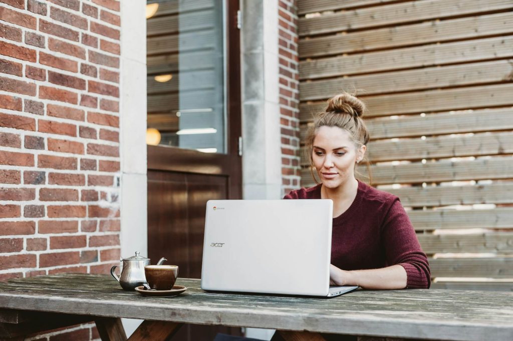 Woman sitting at a wooden table outdoors on a porch, using an acer laptop